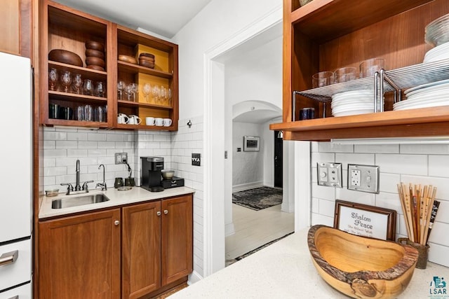 bar with a sink, arched walkways, freestanding refrigerator, and tasteful backsplash