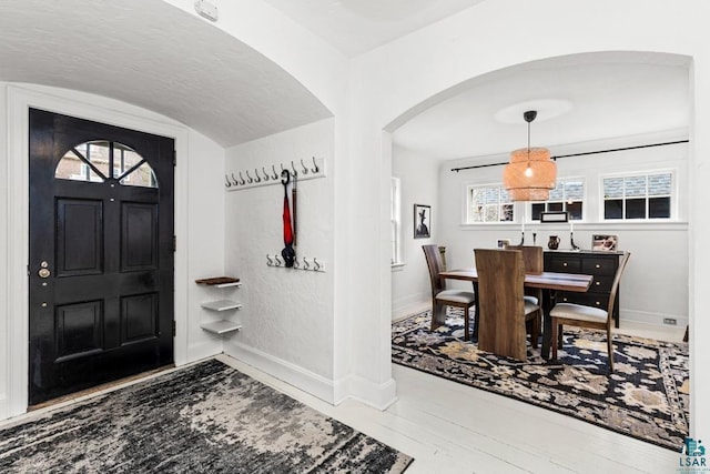 entryway with arched walkways, baseboards, and a wealth of natural light