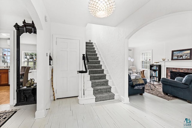 entryway with stairs, a fireplace, baseboards, light wood-type flooring, and arched walkways