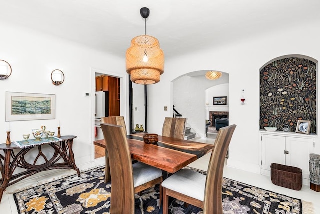 dining area featuring arched walkways, a fireplace, and stairway