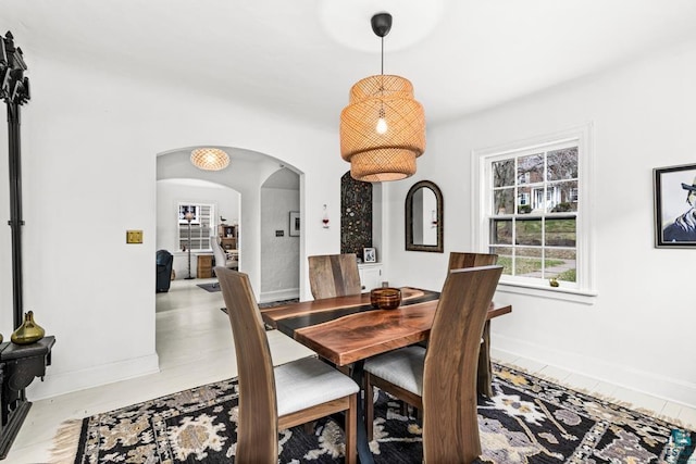 dining area featuring arched walkways, baseboards, and wood finished floors
