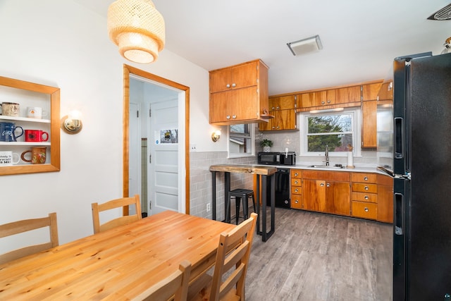 kitchen featuring a sink, light wood-style floors, brown cabinetry, and black appliances