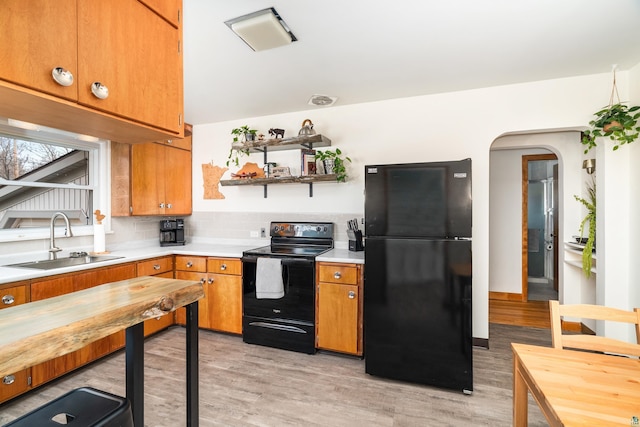 kitchen with light wood-style floors, a sink, brown cabinets, and black appliances