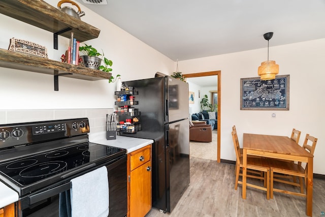 kitchen featuring open shelves, brown cabinets, light wood-type flooring, light countertops, and black appliances