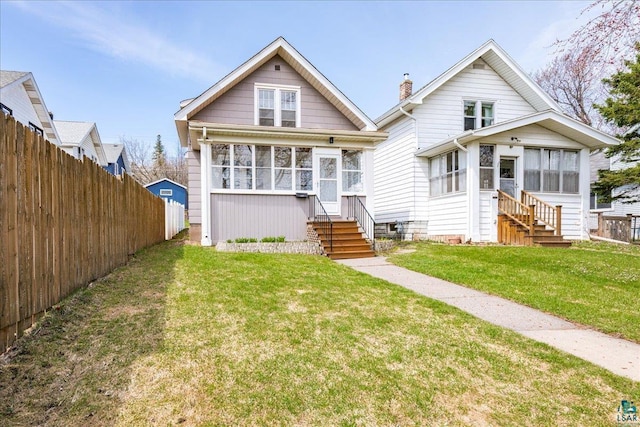 bungalow with fence, a sunroom, a front yard, entry steps, and a chimney