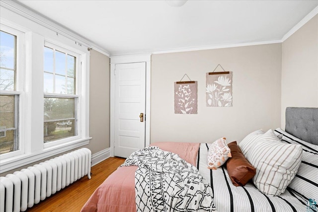 bedroom featuring crown molding, baseboards, light wood finished floors, and radiator heating unit
