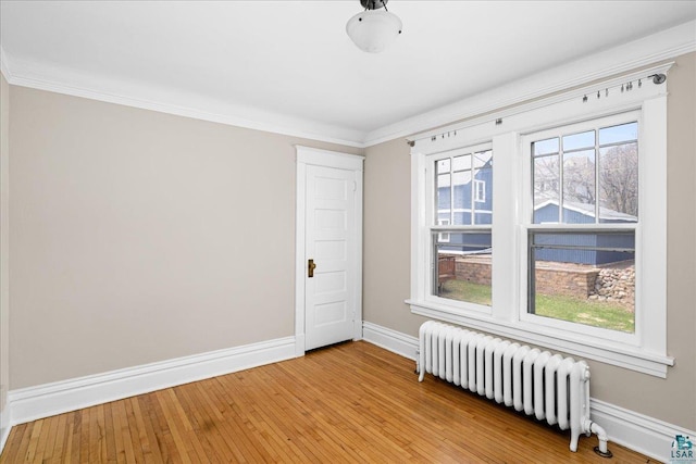 empty room featuring radiator heating unit, baseboards, crown molding, and light wood-style floors