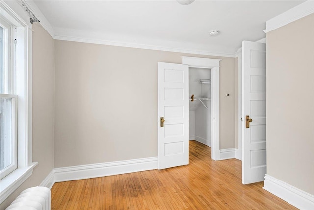unfurnished bedroom with a walk in closet, baseboards, light wood-style flooring, and radiator