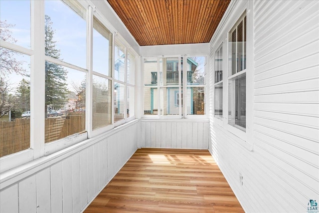 unfurnished sunroom with wooden walls, wood ceiling, a wealth of natural light, and wood finished floors