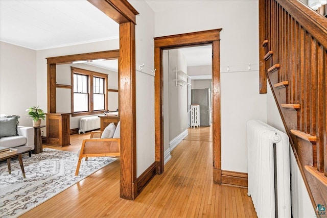 corridor featuring radiator heating unit, baseboards, crown molding, and light wood-style floors