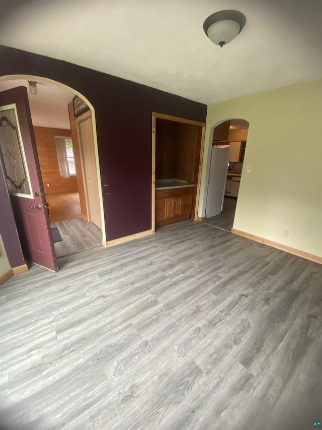 unfurnished living room with wood finished floors, baseboards, and arched walkways