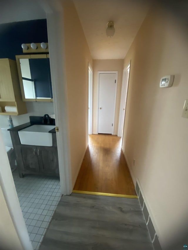 hallway featuring a sink, baseboards, visible vents, and wood finished floors
