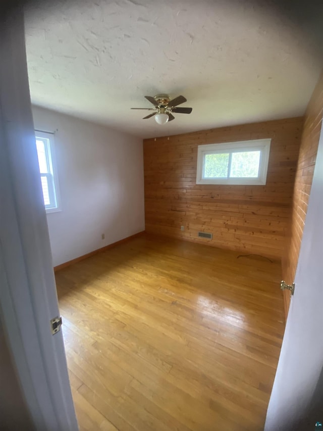 spare room with light wood finished floors, wooden walls, a healthy amount of sunlight, and ceiling fan