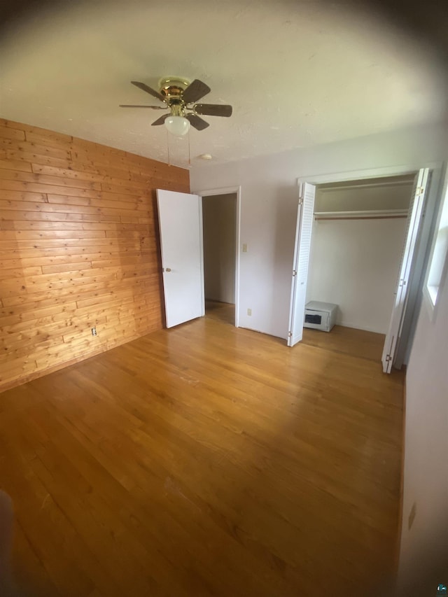 unfurnished bedroom featuring light wood finished floors, a closet, wooden walls, and ceiling fan