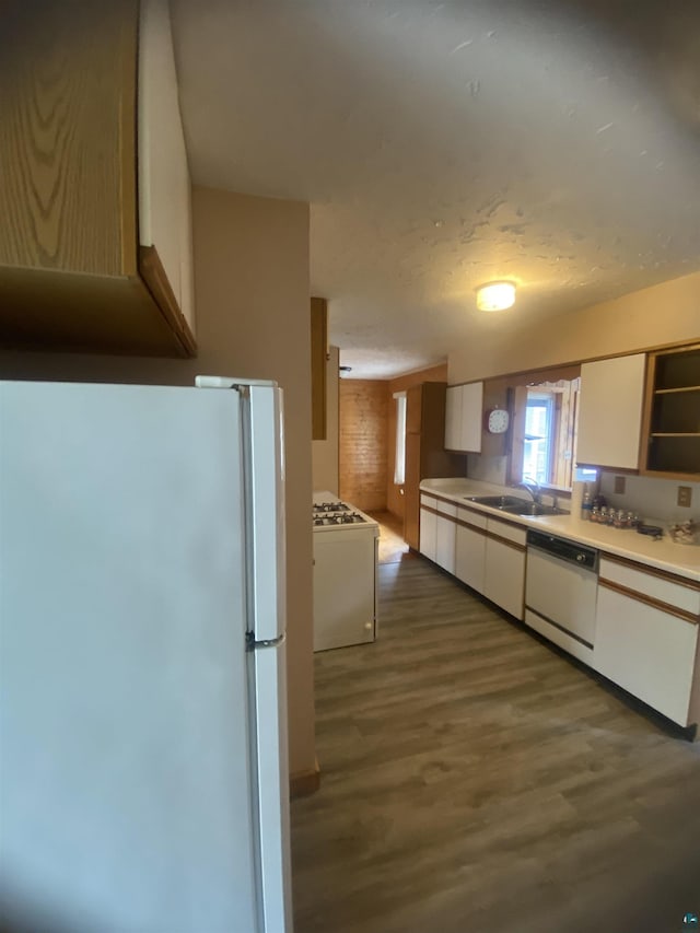 kitchen with dark wood-style flooring, white appliances, a sink, light countertops, and white cabinets
