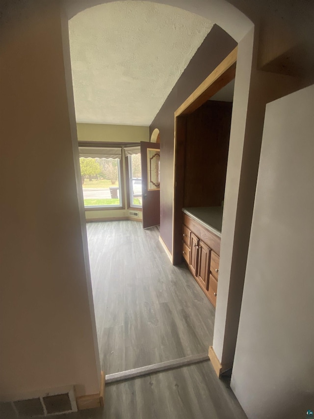 hallway featuring a textured ceiling, wood finished floors, baseboards, and arched walkways