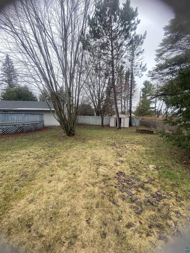 view of yard featuring fence, an outdoor structure, a deck, and a storage unit