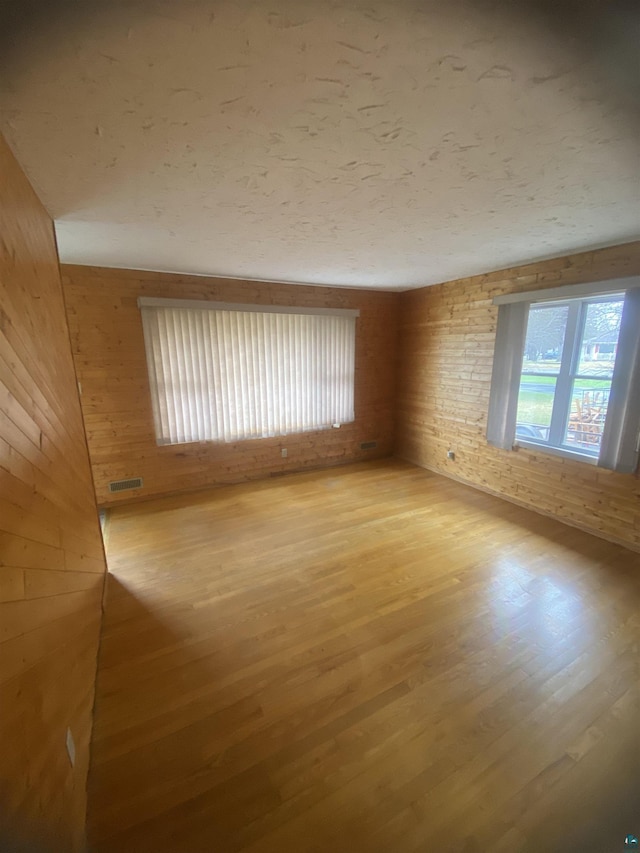 unfurnished room with light wood-style flooring, wooden walls, and visible vents
