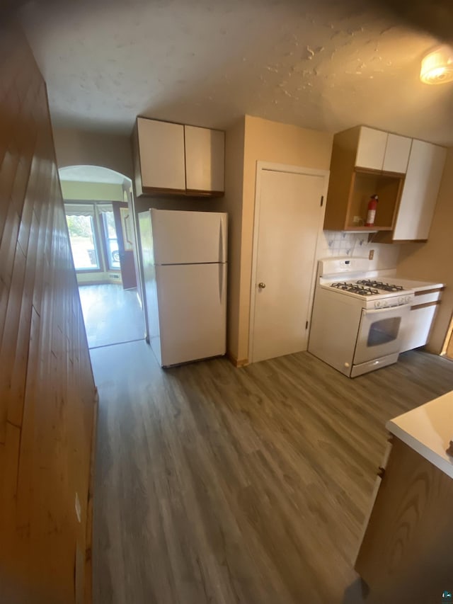 kitchen with white appliances, arched walkways, white cabinets, and wood finished floors