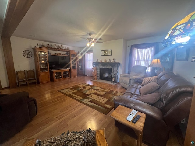 living room with a ceiling fan, a stone fireplace, plenty of natural light, and wood finished floors
