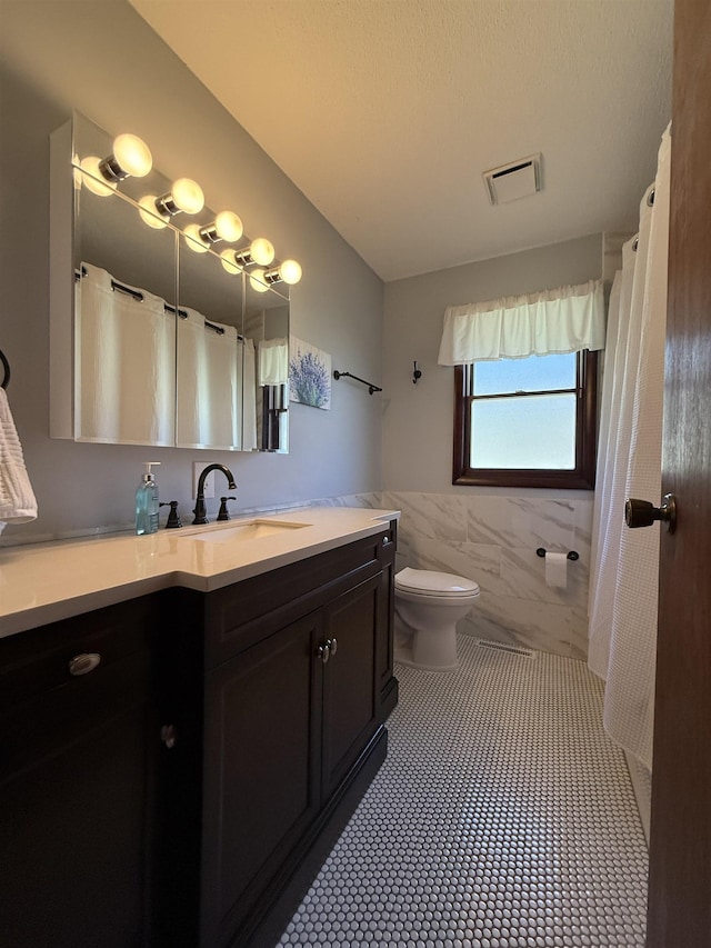46040 State Highway 65, Nashwauk, MN 55769 - full bath with toilet, a wainscoted wall, tile walls, visible vents, and vanity