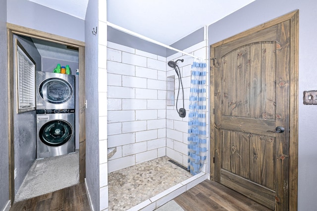 full bath with stacked washer and dryer, tiled shower, and wood finished floors