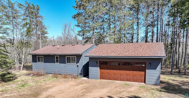 view of front facade with dirt driveway, a shingled roof, and a garage