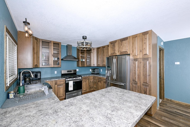 kitchen with a peninsula, a chandelier, dark wood-type flooring, wall chimney range hood, and stainless steel appliances