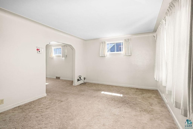 carpeted empty room featuring arched walkways, baseboards, and visible vents