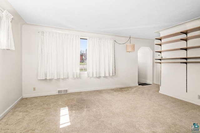 below grade area with carpet floors, baseboards, visible vents, and arched walkways