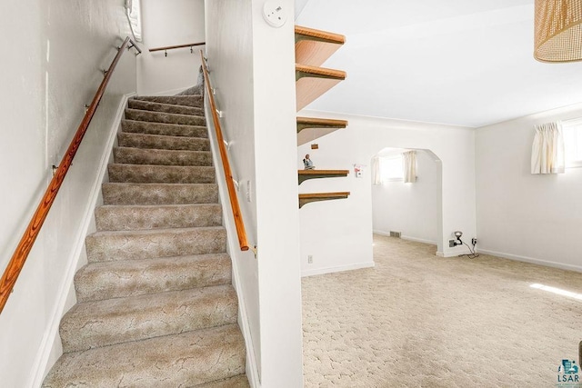 stairway featuring arched walkways and carpet flooring