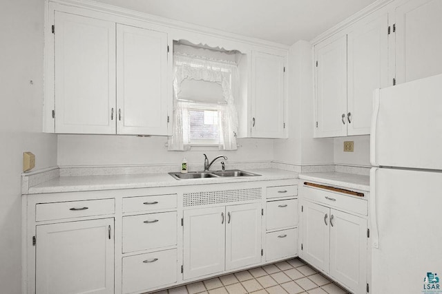kitchen with freestanding refrigerator, light countertops, white cabinets, and a sink