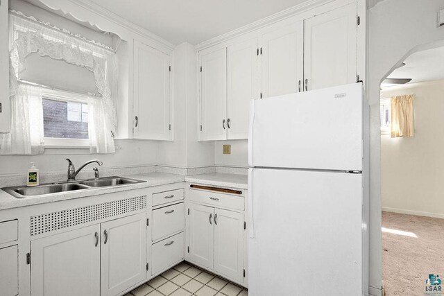kitchen featuring freestanding refrigerator, light countertops, white cabinetry, and a sink