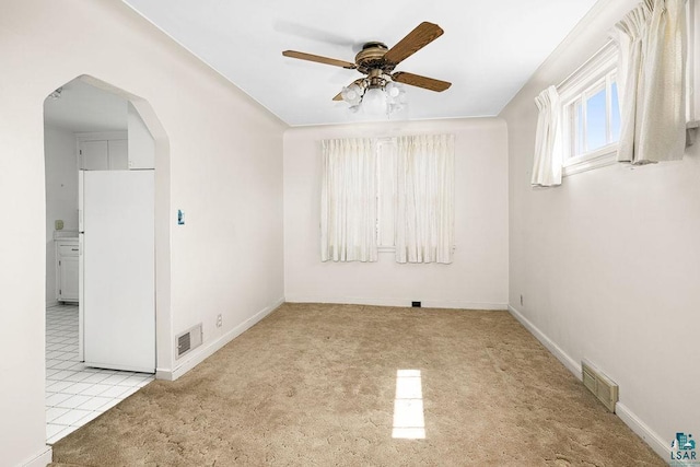carpeted spare room with a ceiling fan, baseboards, visible vents, and arched walkways