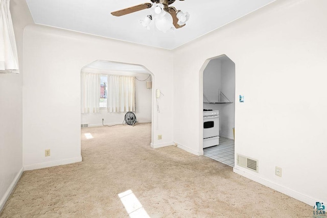 empty room featuring baseboards, ceiling fan, visible vents, arched walkways, and carpet floors