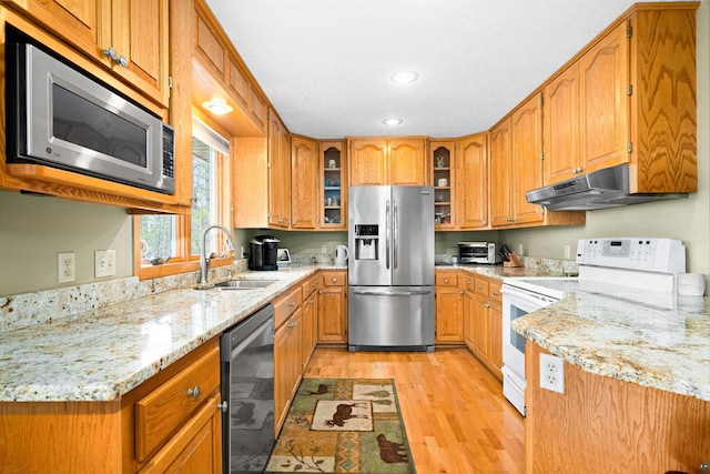 kitchen featuring light wood finished floors, a sink, stainless steel appliances, under cabinet range hood, and light stone counters