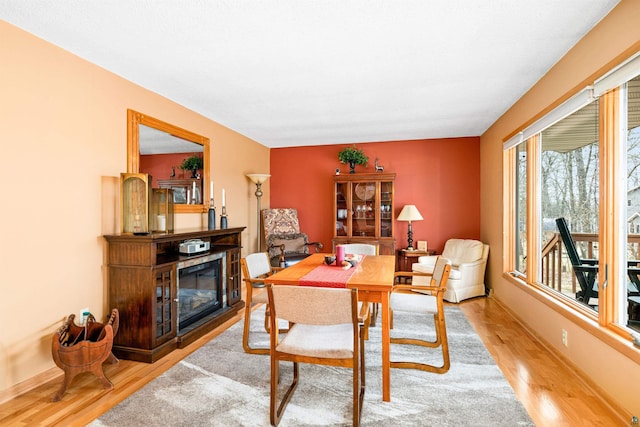 dining space with light wood-style floors, baseboards, and a glass covered fireplace