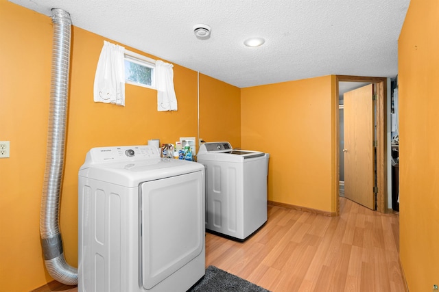 clothes washing area featuring washer and clothes dryer, laundry area, a textured ceiling, and light wood-style flooring
