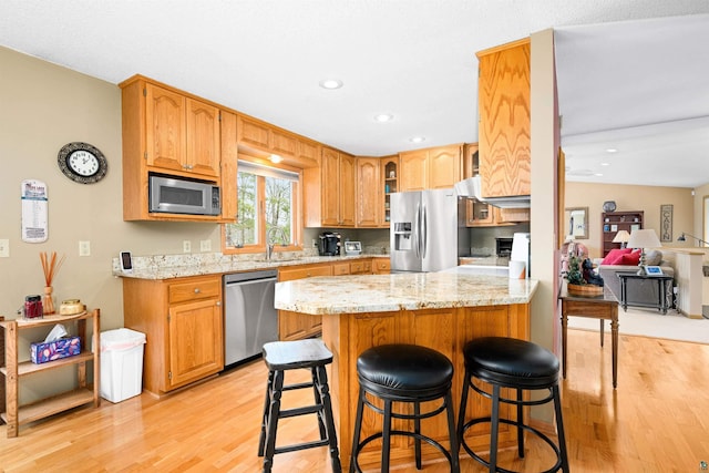 kitchen featuring a peninsula, light wood-style flooring, glass insert cabinets, light stone countertops, and appliances with stainless steel finishes