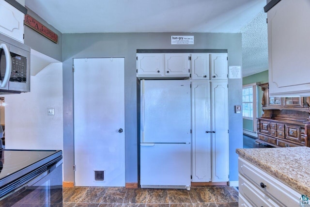 kitchen with freestanding refrigerator, white cabinets, stainless steel microwave, a baseboard heating unit, and range with electric stovetop