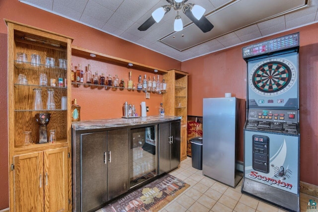 bar with a dry bar, freestanding refrigerator, stacked washer / drying machine, ceiling fan, and light tile patterned floors