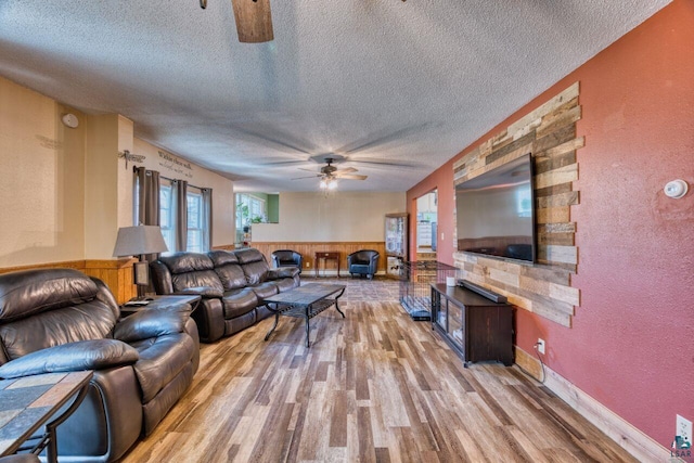 living room with a wainscoted wall, a textured ceiling, light wood-type flooring, a textured wall, and a ceiling fan
