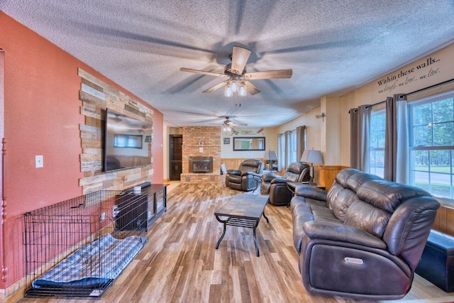 living room featuring a textured ceiling, ceiling fan, a brick fireplace, wood finished floors, and a textured wall