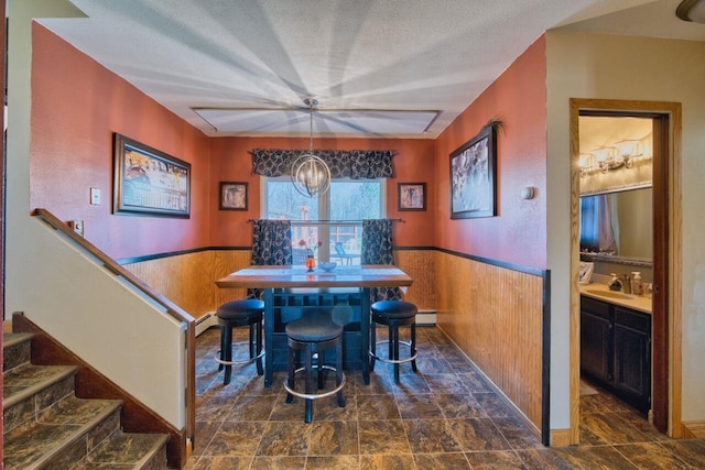 dining space featuring wood walls, wainscoting, stone finish floor, and a notable chandelier