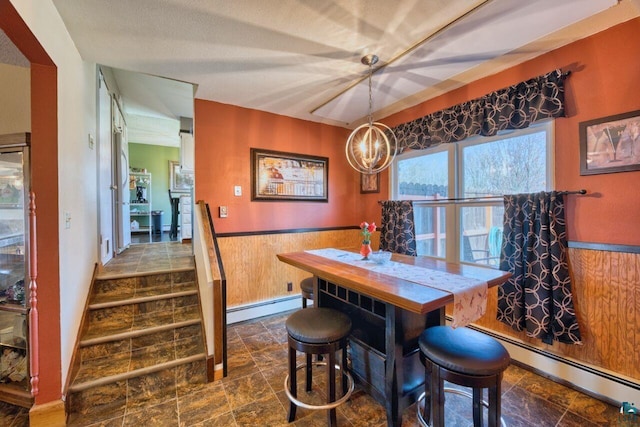 dining room with a notable chandelier, a baseboard radiator, stone finish flooring, and a wainscoted wall