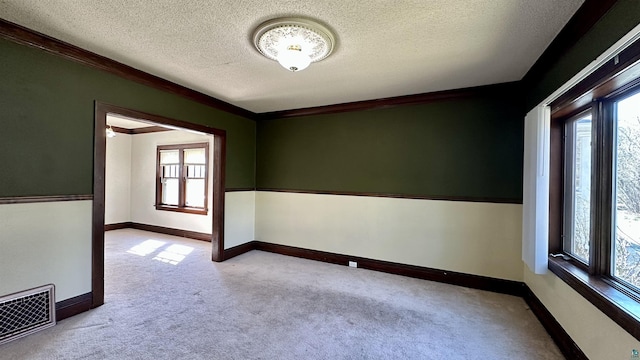 carpeted empty room with plenty of natural light, a textured ceiling, baseboards, and crown molding