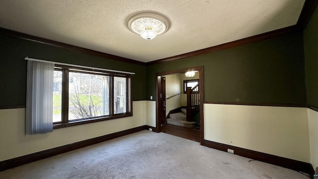 carpeted spare room with stairs, a textured ceiling, baseboards, and ornamental molding