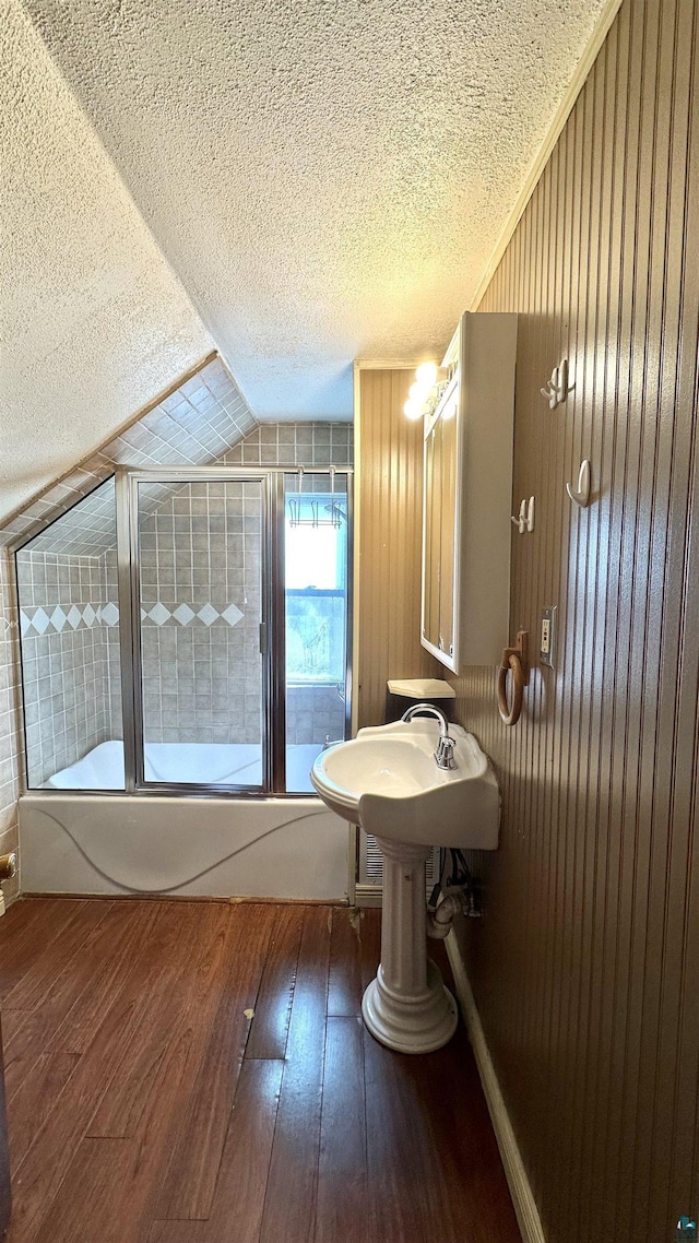 bathroom with hardwood / wood-style floors, a textured ceiling, vaulted ceiling, and combined bath / shower with glass door