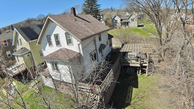 view of side of home with roof with shingles, a chimney, a residential view, and a lawn