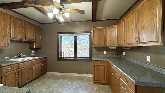 kitchen with a sink, ceiling fan, baseboards, brown cabinets, and beam ceiling
